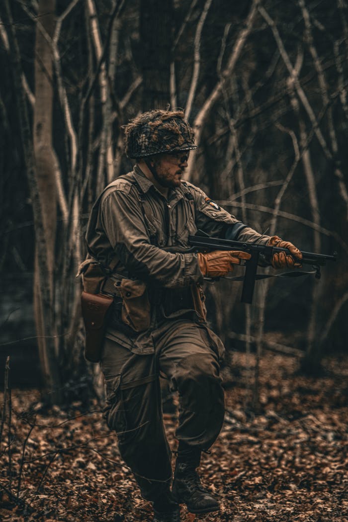 A soldier in camouflage gear walking through a dense forest, holding a firearm.