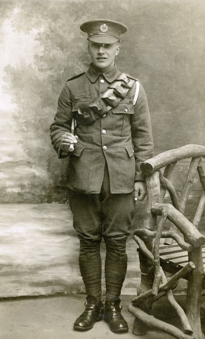 Sepia-toned vintage photo of a soldier in a classic military uniform with a rustic chair.