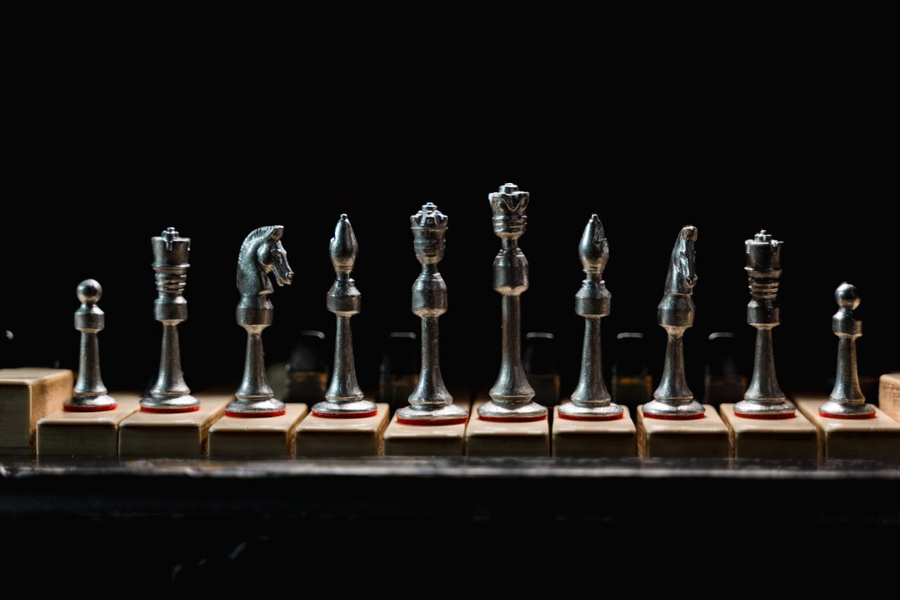 A row of elegant metal chess pieces displayed on wooden blocks against a dark background.